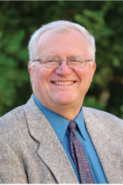 Robert LeBorne outdoors in a gray jacket and blue shirt, smiling at the camera