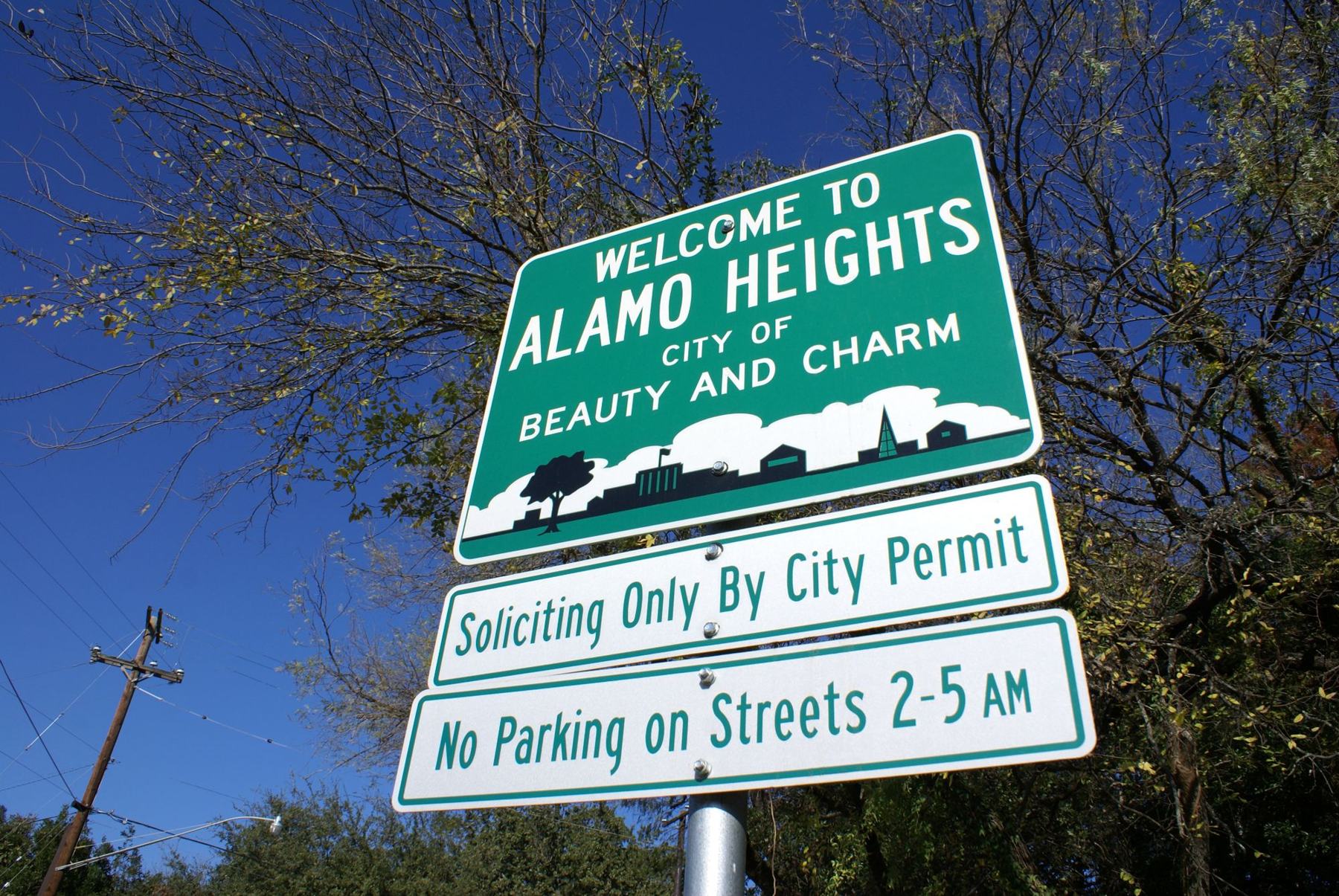 The green Welcome to Alamo Heights sign, City of Beauty and Charm, against a deep blue sky