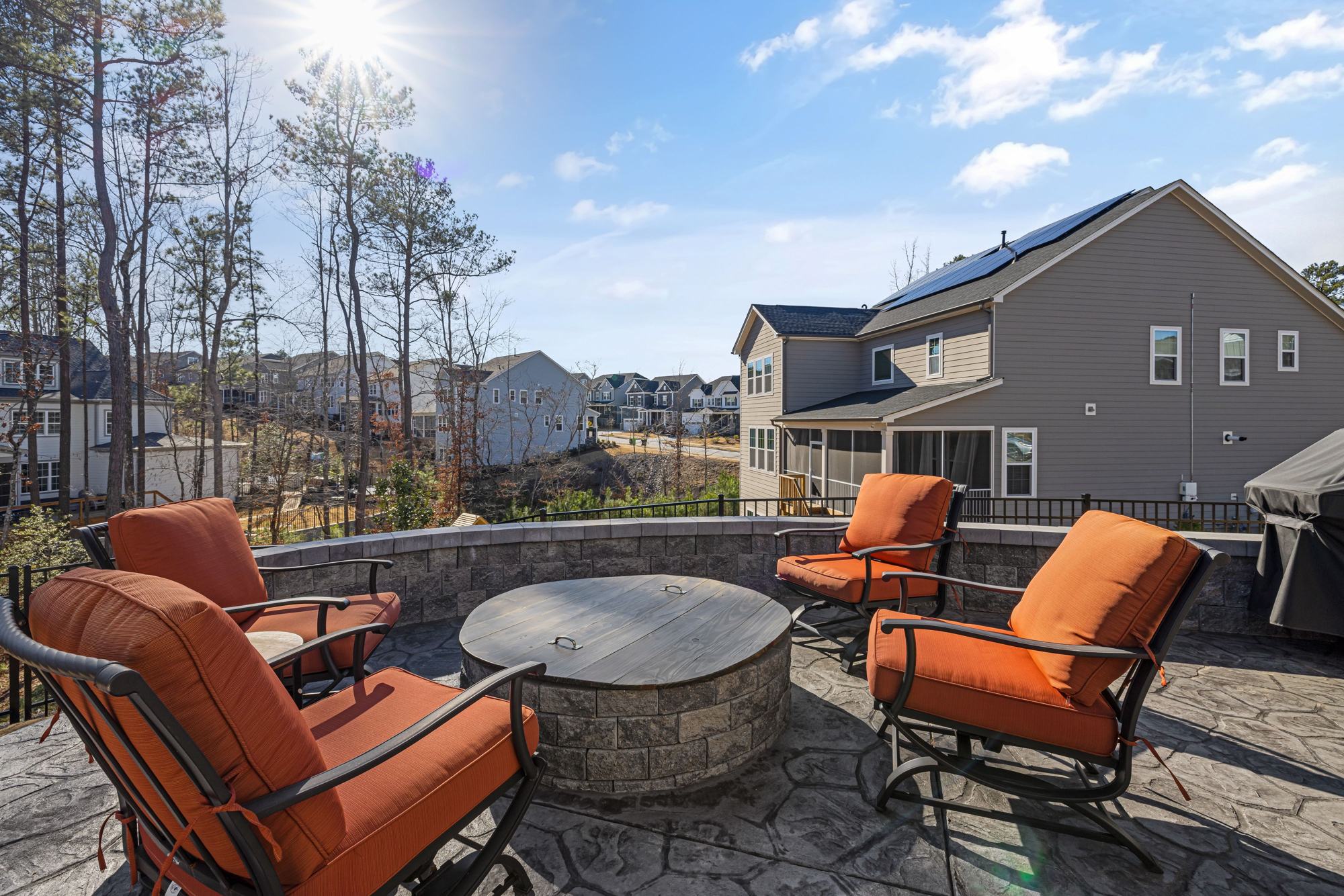 A round stone fire pit ringed by orange patio chairs in a wooded backyard