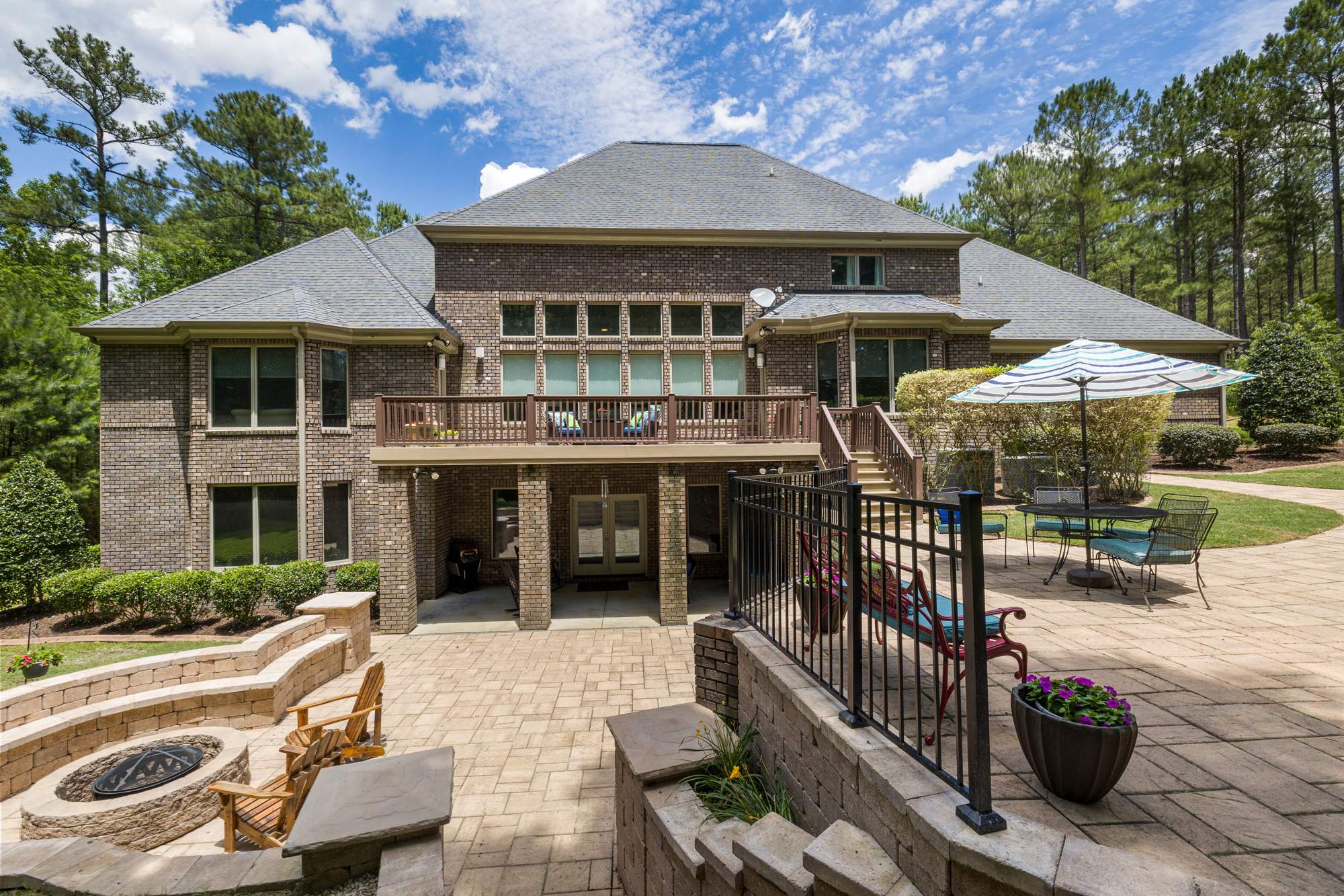 The back of a two-story stone home with a fire pit and a stone patio