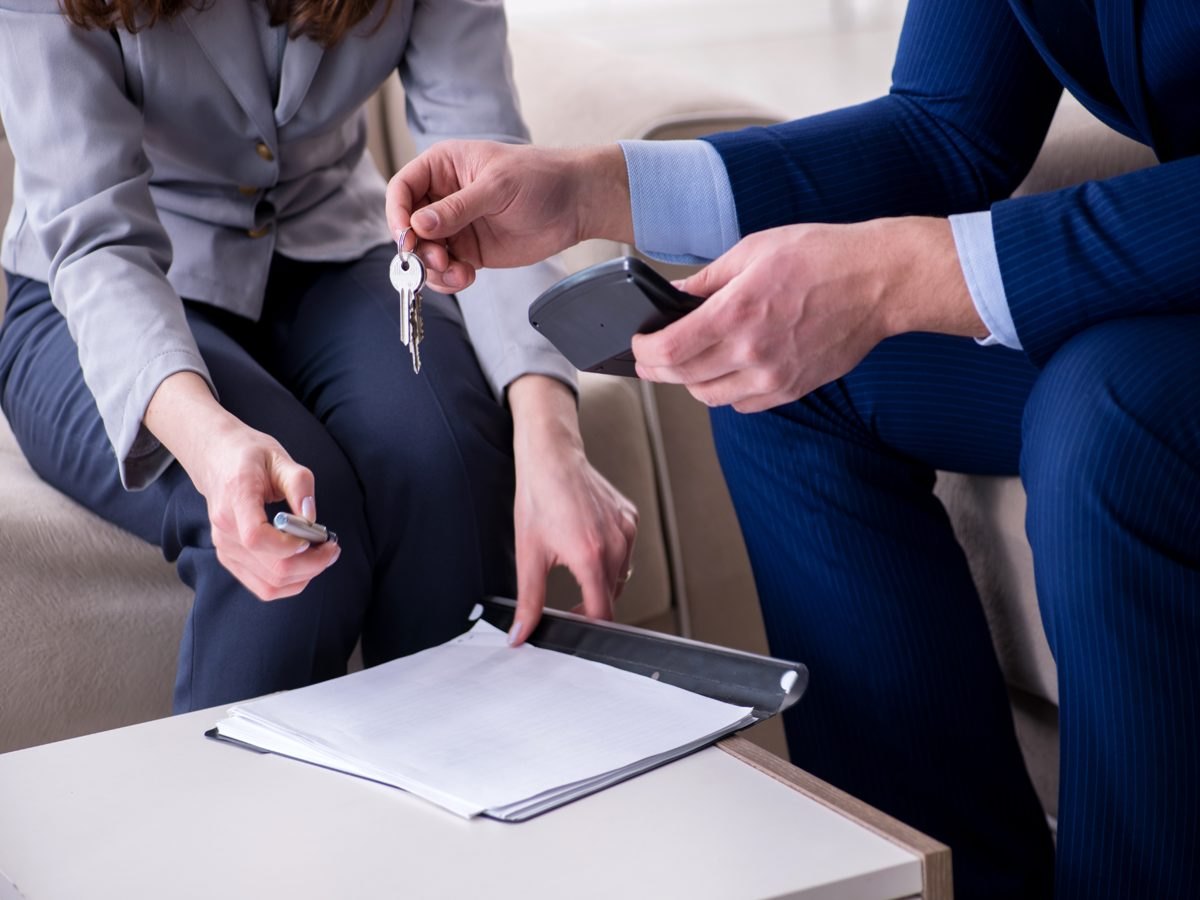 An agent handing house keys across a table to a buyer signing paperwork