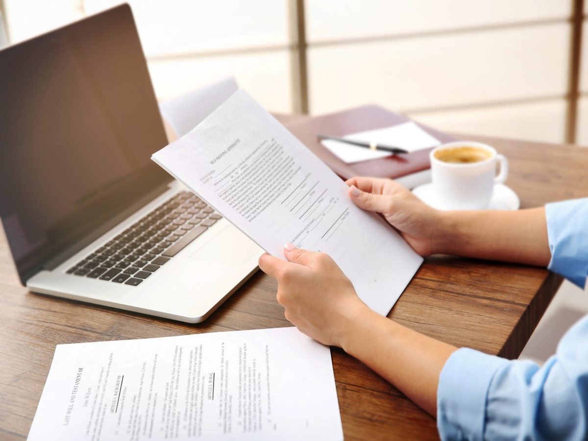 A broker reading through a contract at a desk beside a laptop and notes