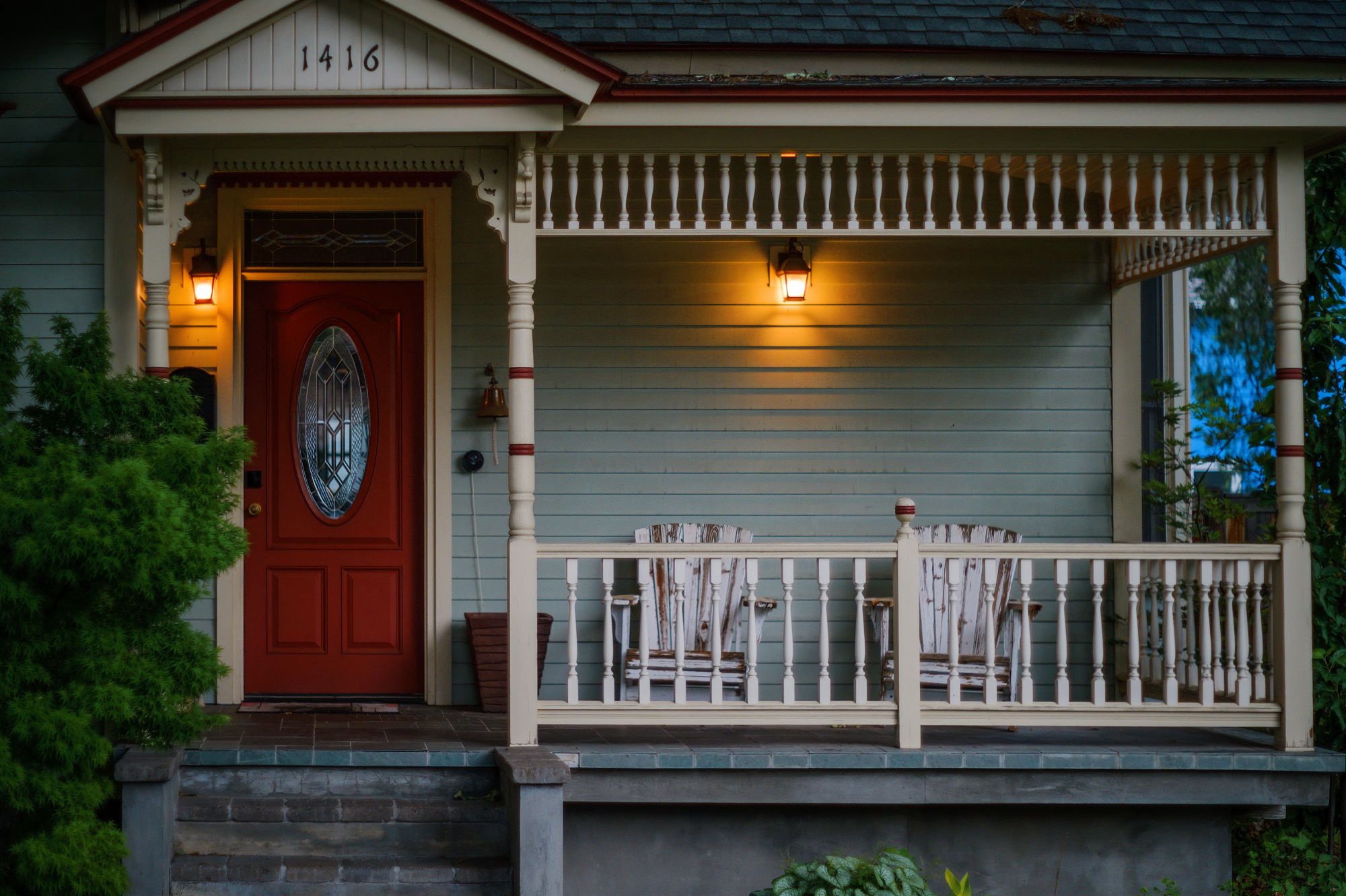 A gray bungalow with a red front door and a white-railed porch