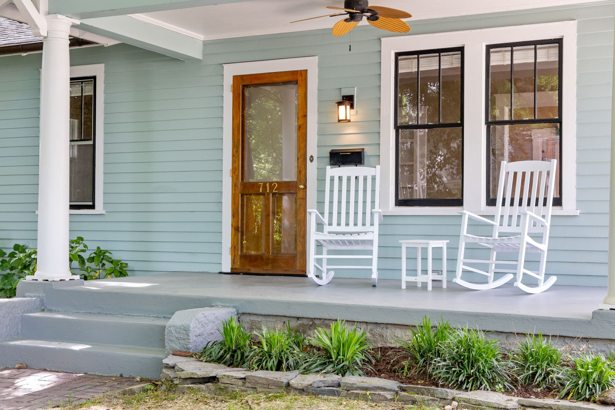 A blue craftsman house with a wood front door and rocking chairs on the porch