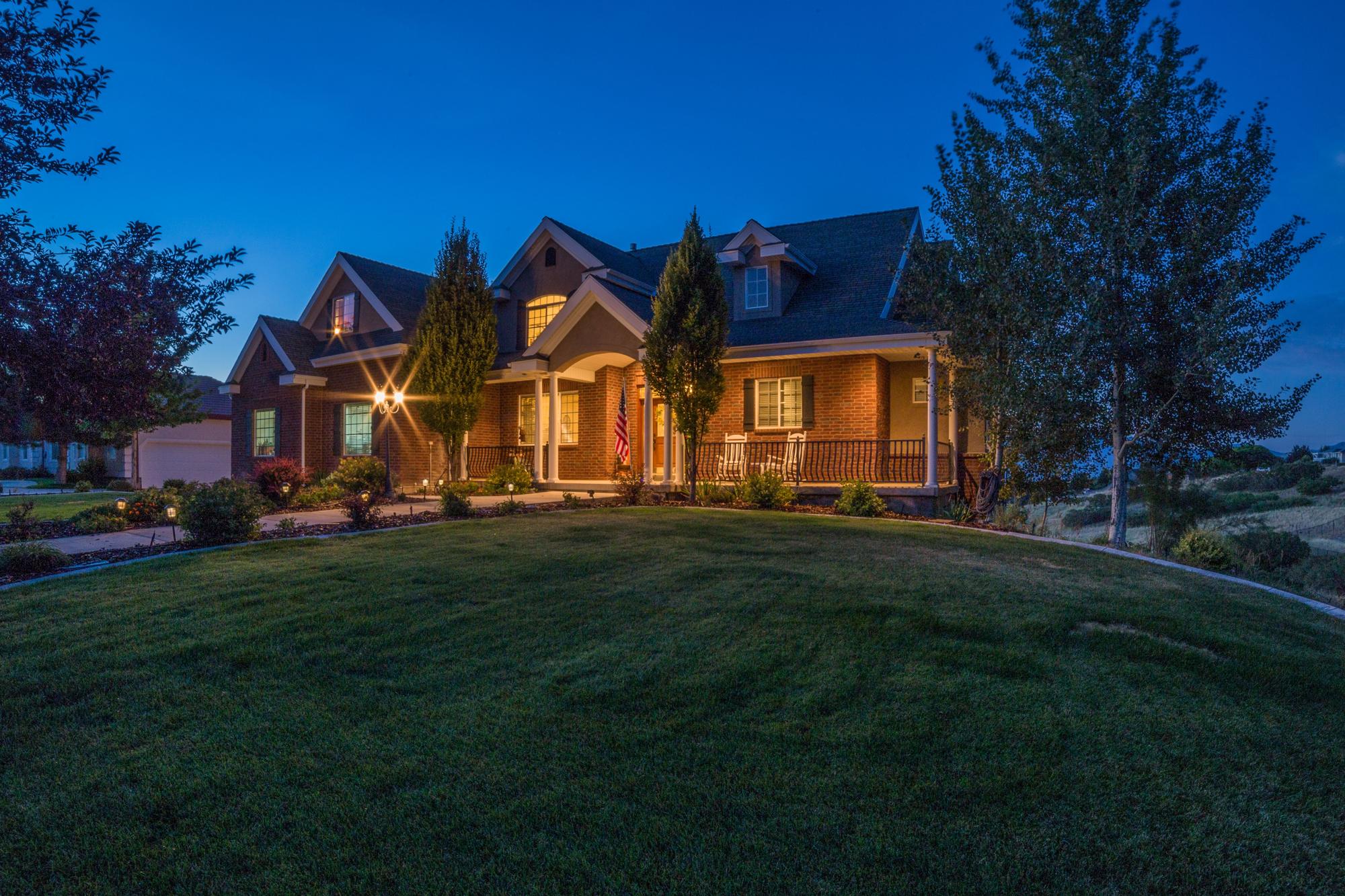 A two-story home at dusk with lit windows above a wide front lawn