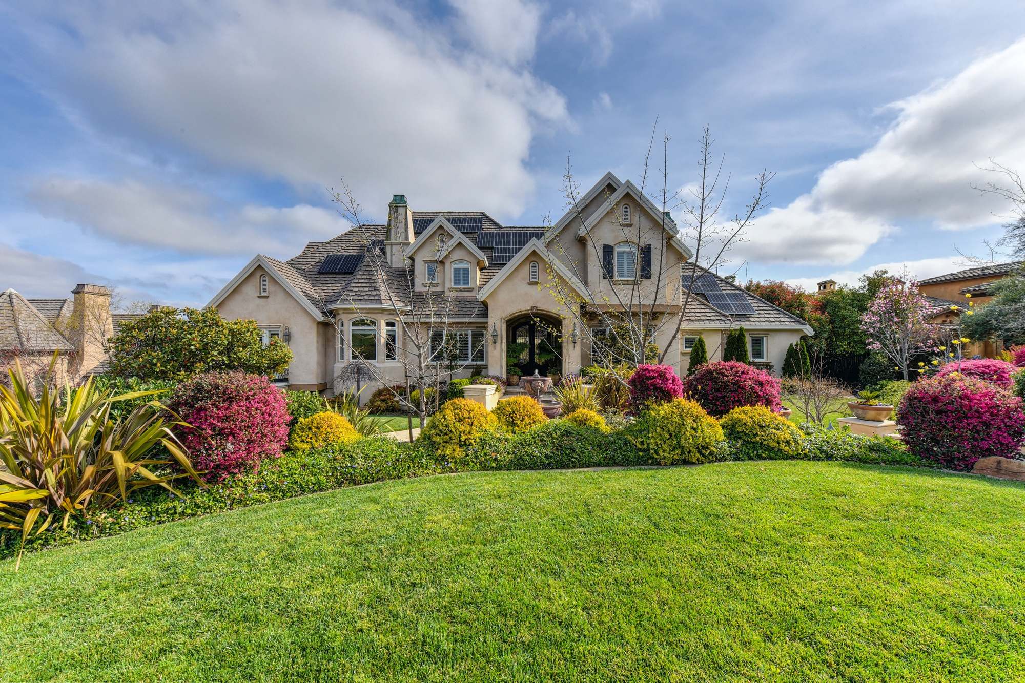 A large stone-trimmed home behind a green lawn and beds of bright flowers