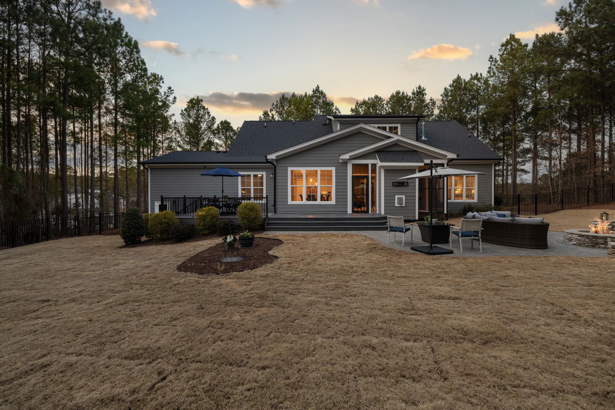 A large home among tall pines at dusk, its windows lit against a deep blue sky