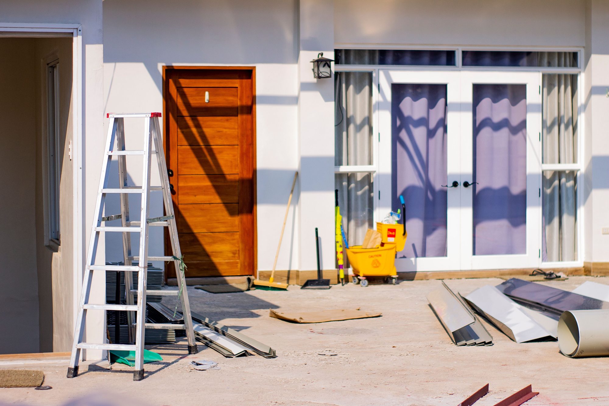A house mid-renovation, with a ladder and building materials outside a freshly painted front door