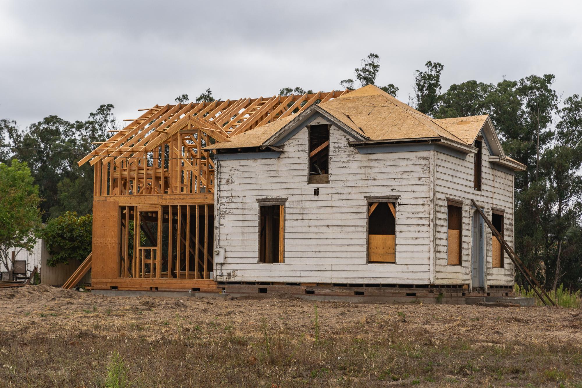 An older frame house with a new timber-framed addition going up beside it