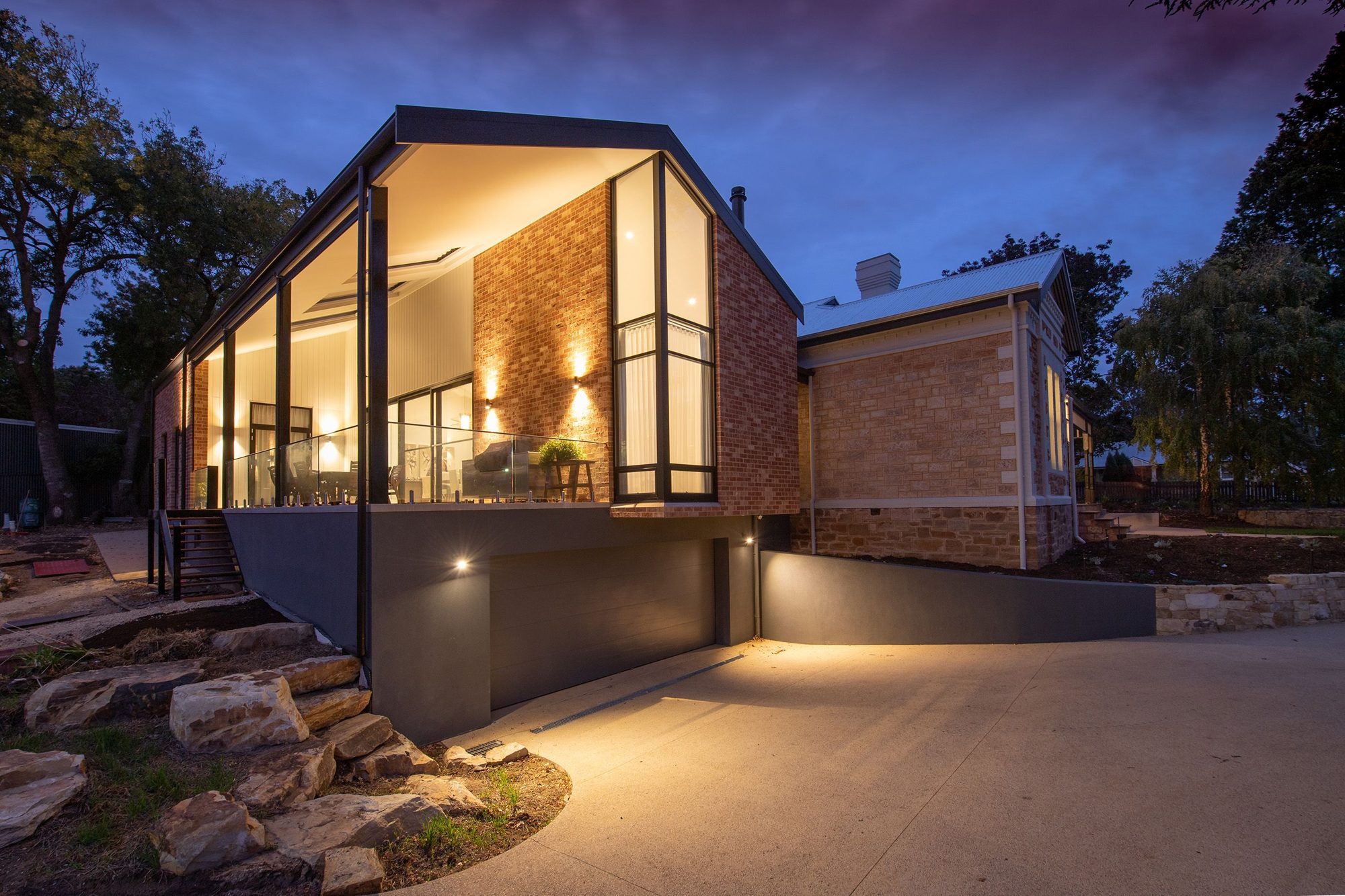 A modern brick and glass home on a stone hillside, lit from inside at dusk