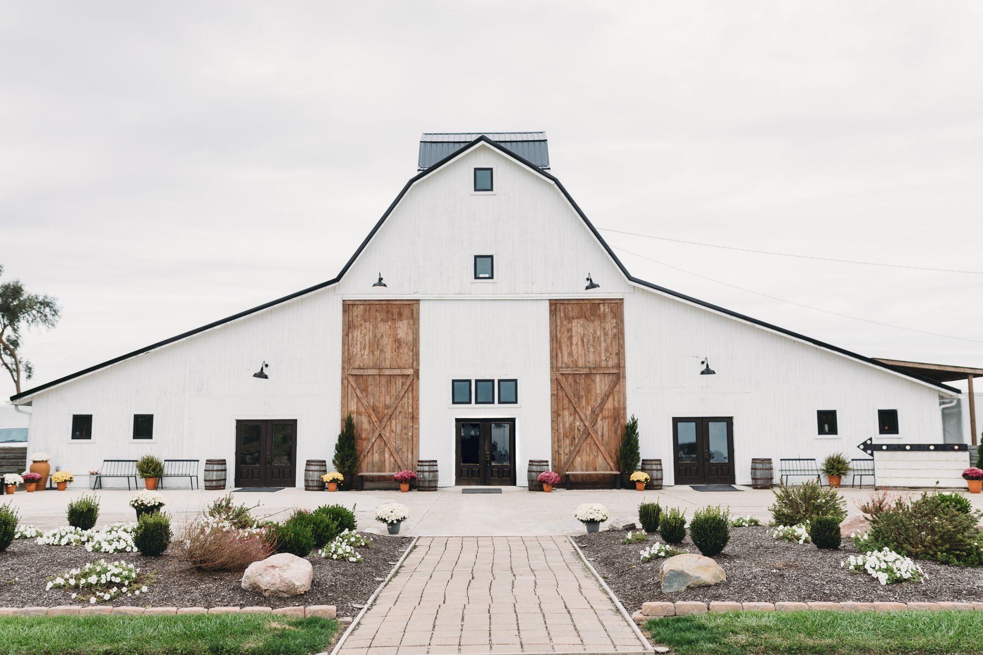 A white modern farmhouse with black barn-style doors and a landscaped front walk