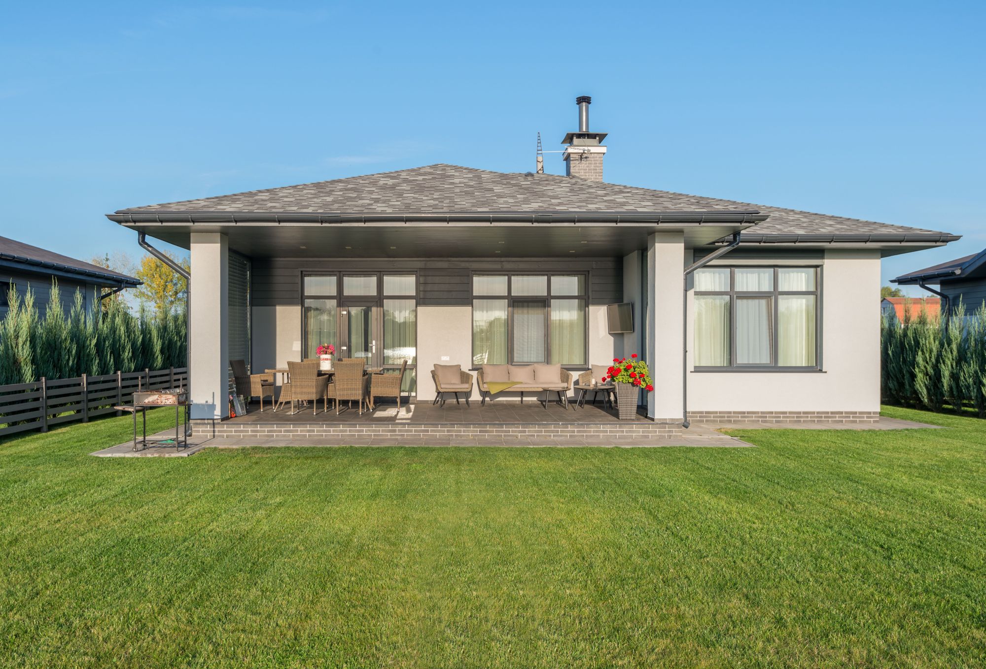 A single-story modern home with a covered patio facing a wide lawn