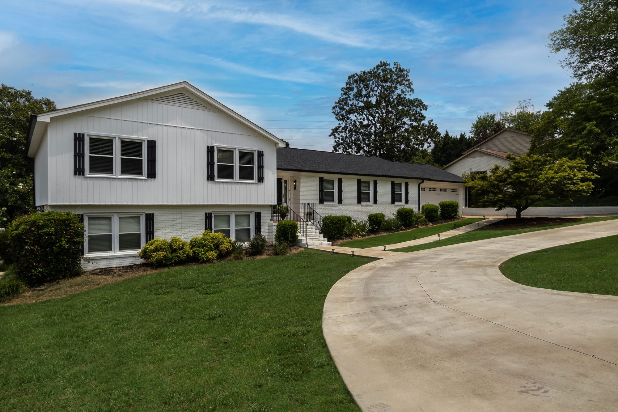 A white ranch home at the end of a long curving driveway and a wide lawn