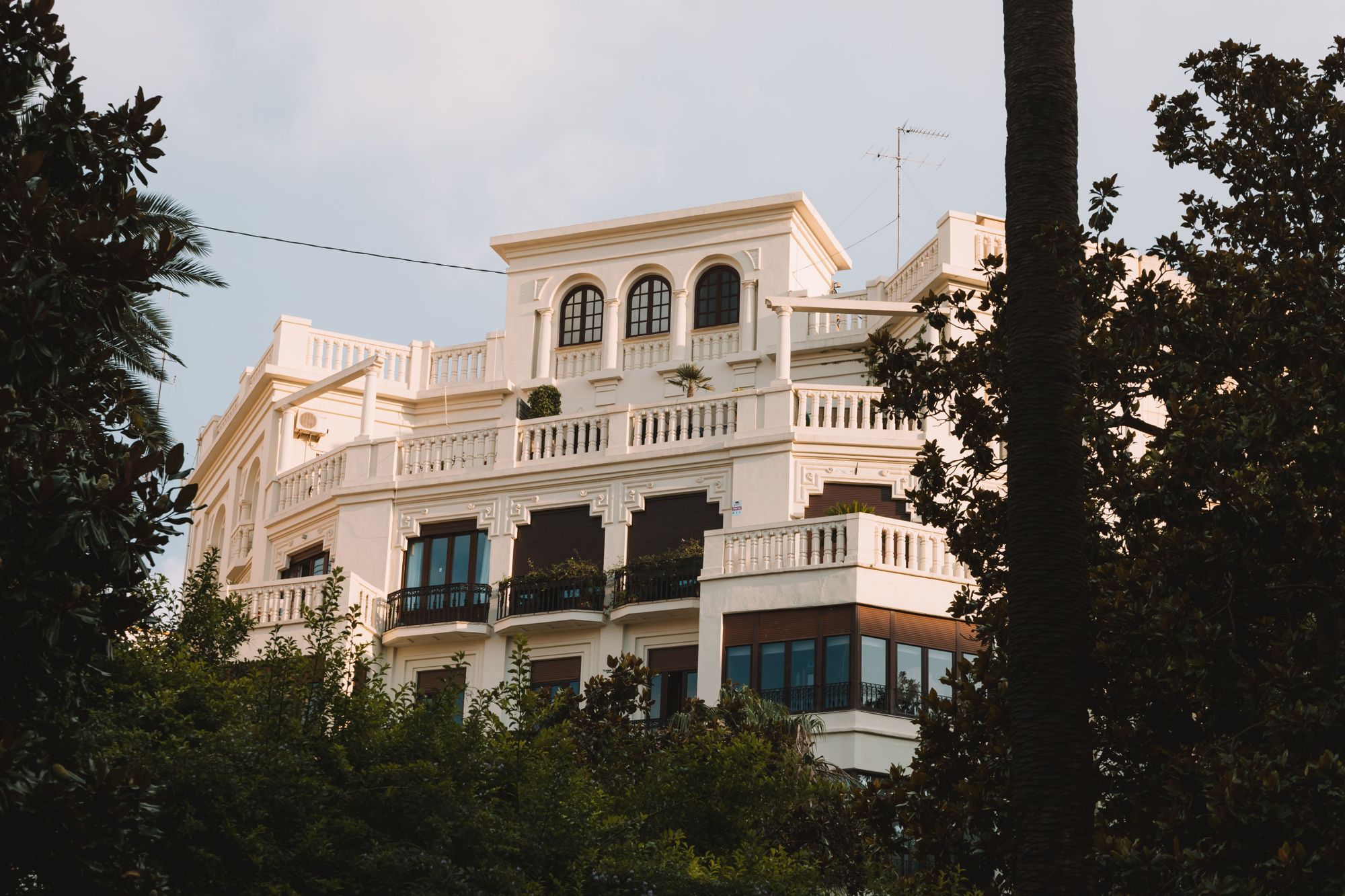 A white revival-style villa with balconies set among mature trees