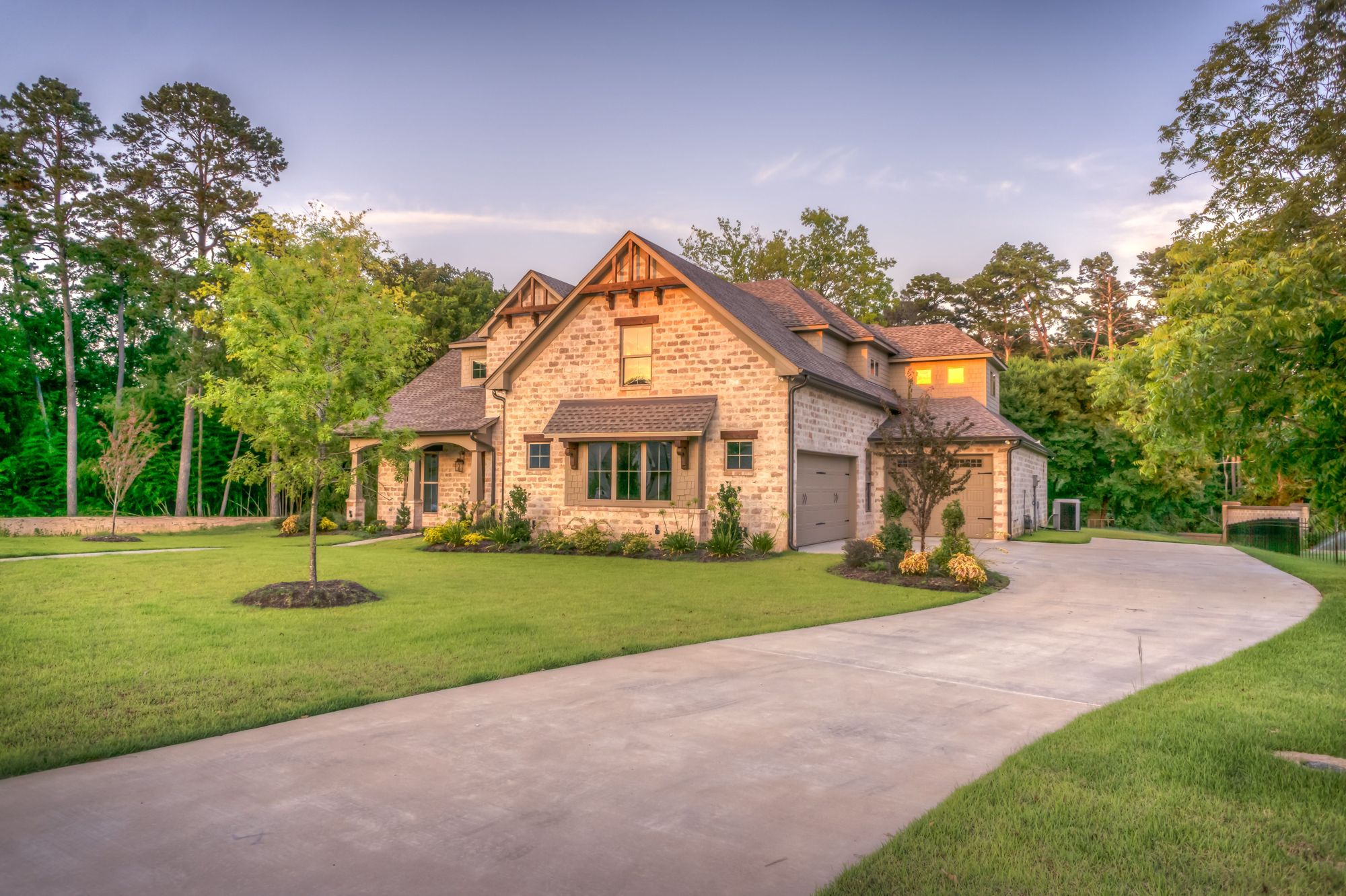 A large stone home at the end of a curving drive, framed by tall trees