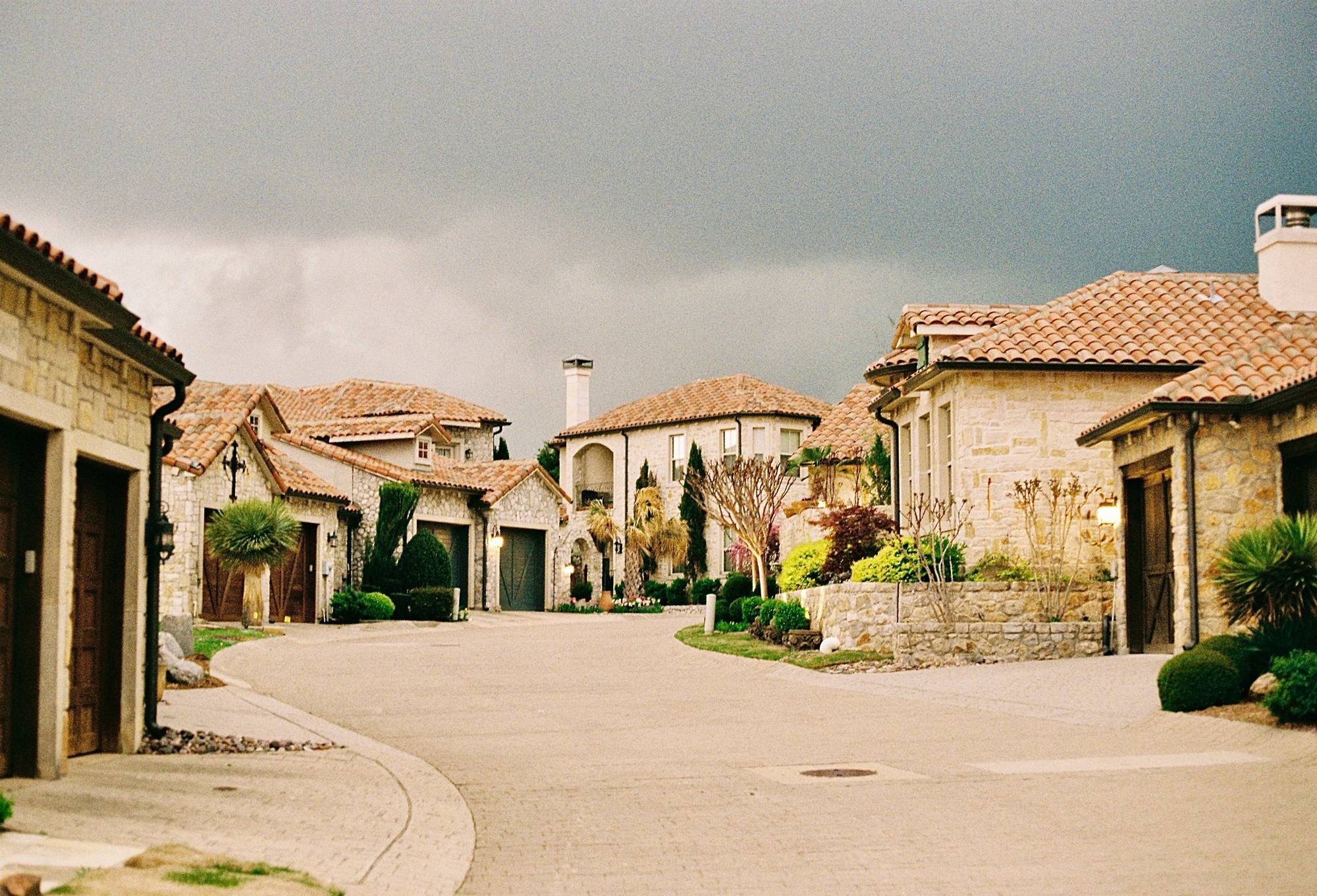 Stone homes with tile roofs around a quiet cul-de-sac, framed by cypress trees