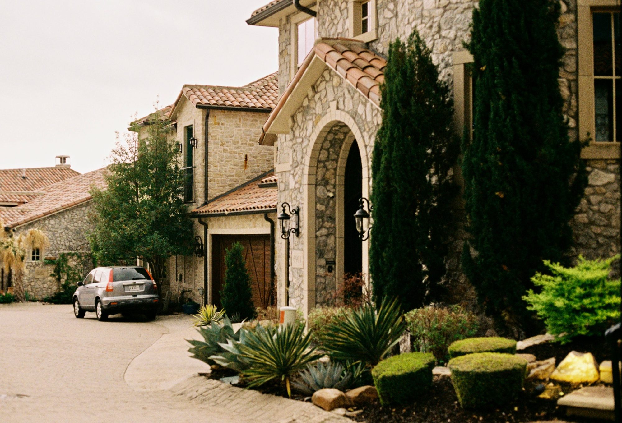 A Tuscan-style stone home with arched windows, cypress trees and agave in the front beds