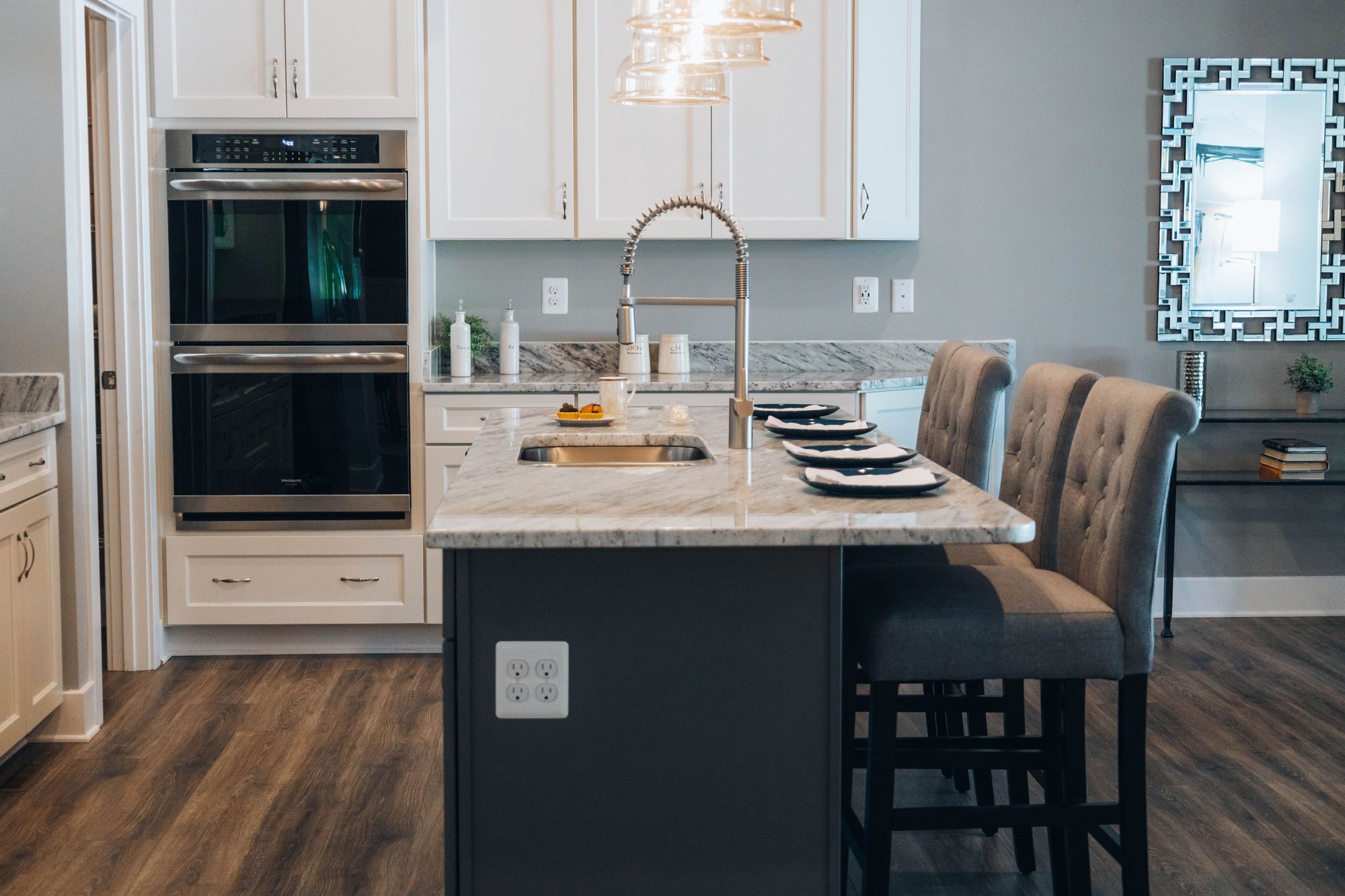 A white kitchen with a dark island, double ovens and wood floors