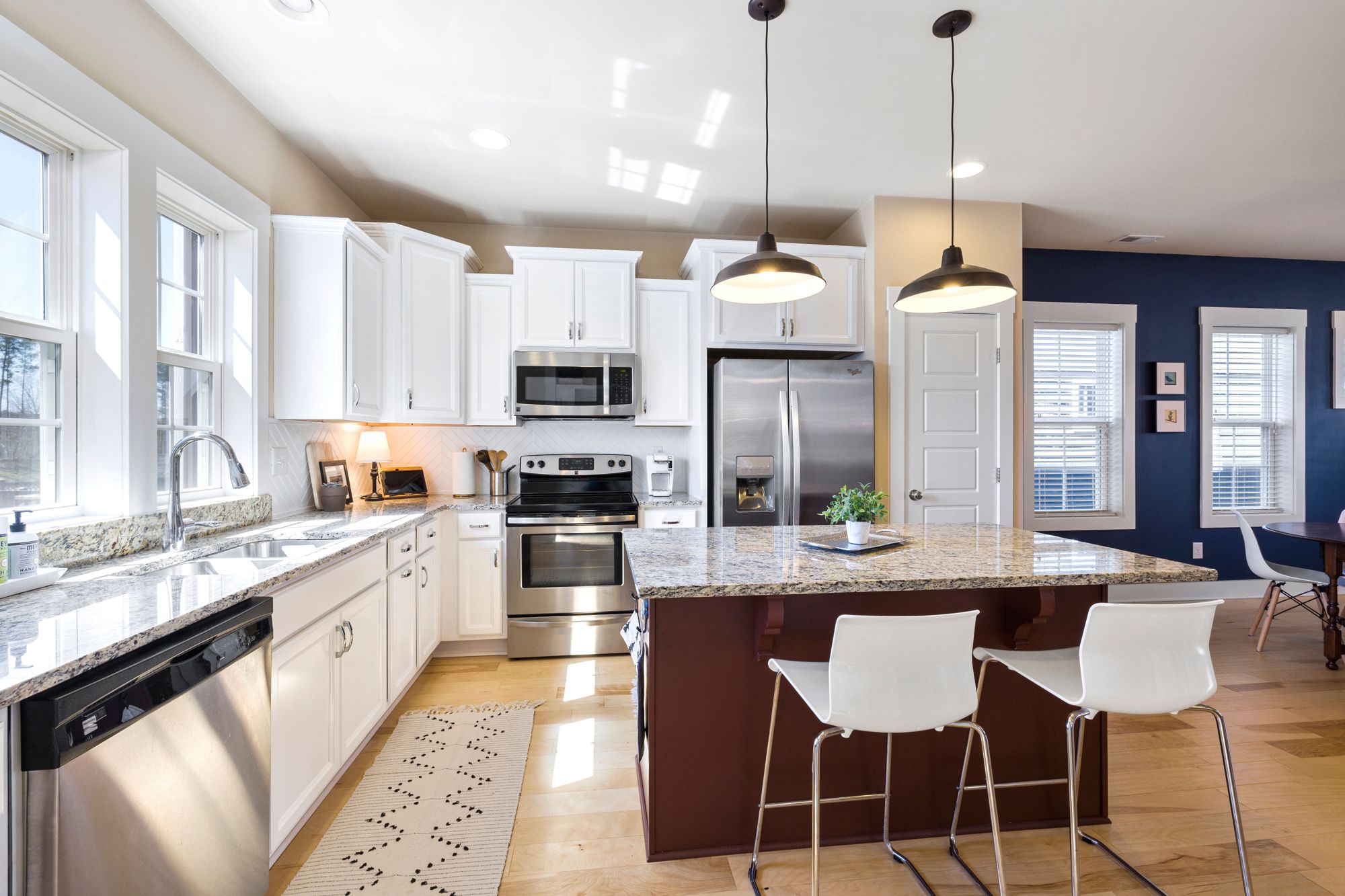 A kitchen with a long island, white cabinets and black pendant lights