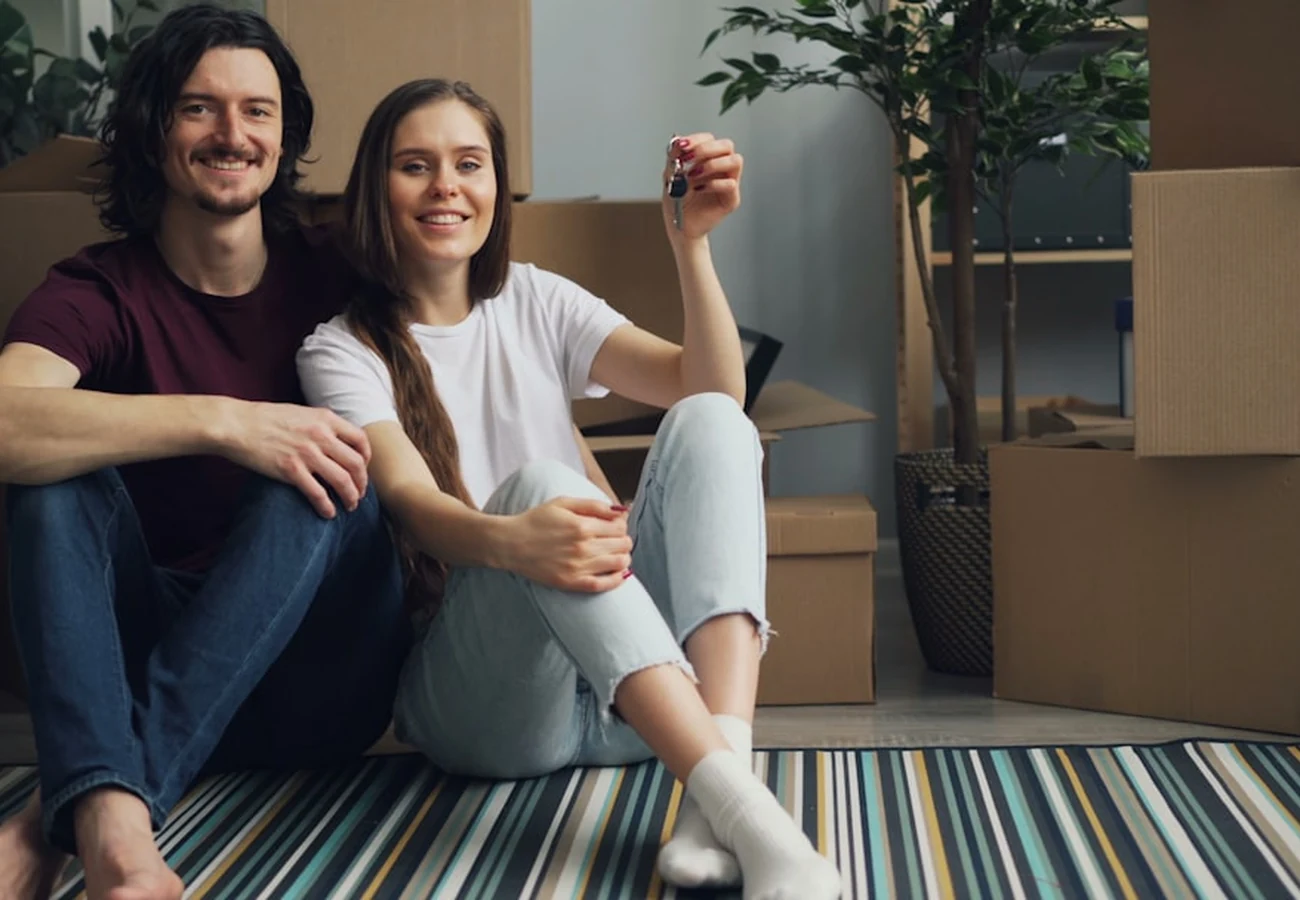 A smiling couple sitting on the floor of their new home holding up the keys