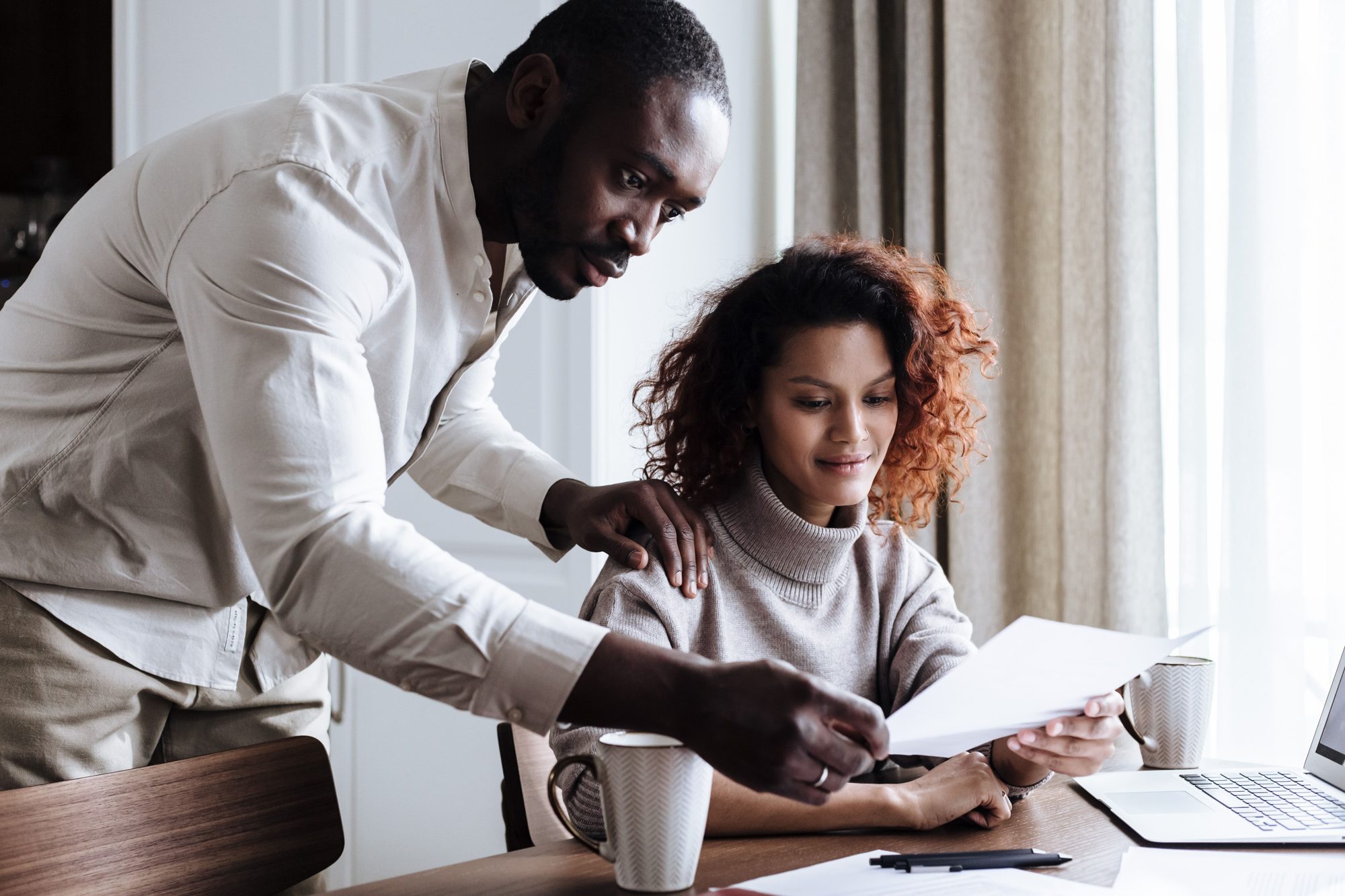 A couple reading through financial documents together at a kitchen table with a laptop