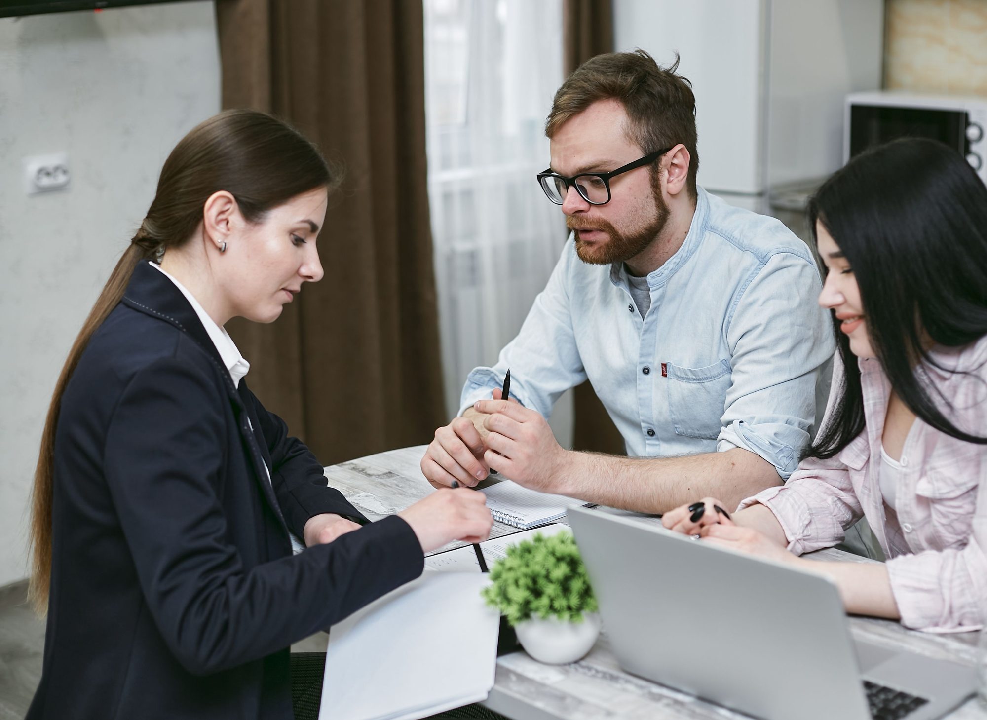 A real estate professional reviewing figures on a laptop with a couple at a dining table