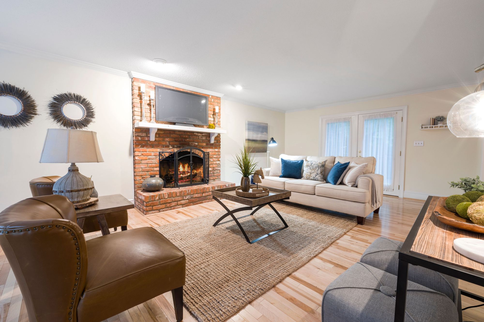 A living room with a brick fireplace, a leather sofa and wood floors