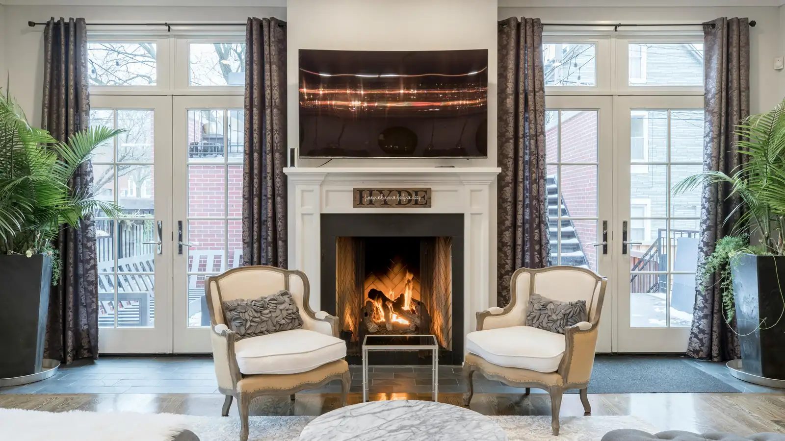 A formal living room with a lit fireplace between two sets of French doors