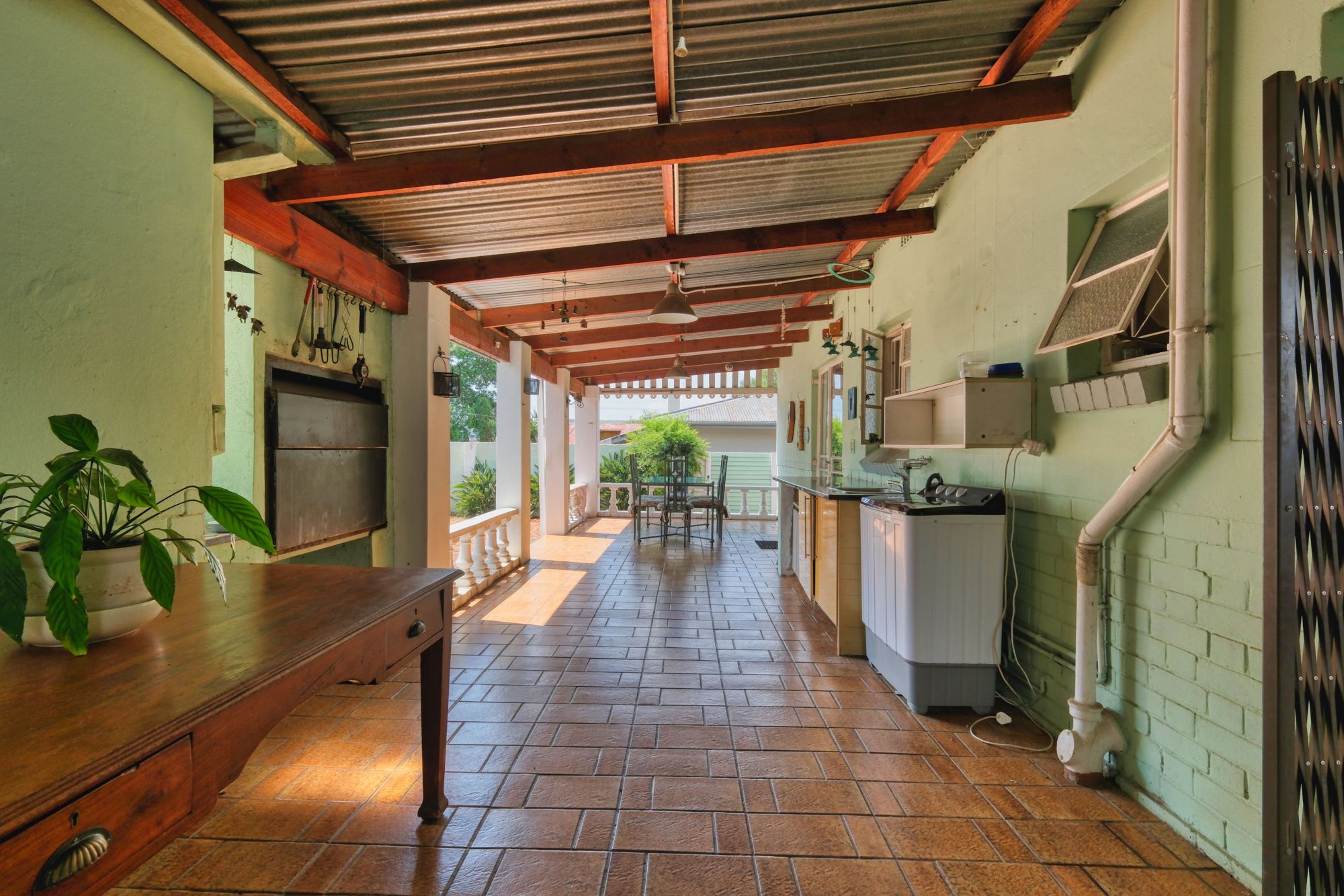 A covered outdoor kitchen and dining area with a tile floor and wood beams