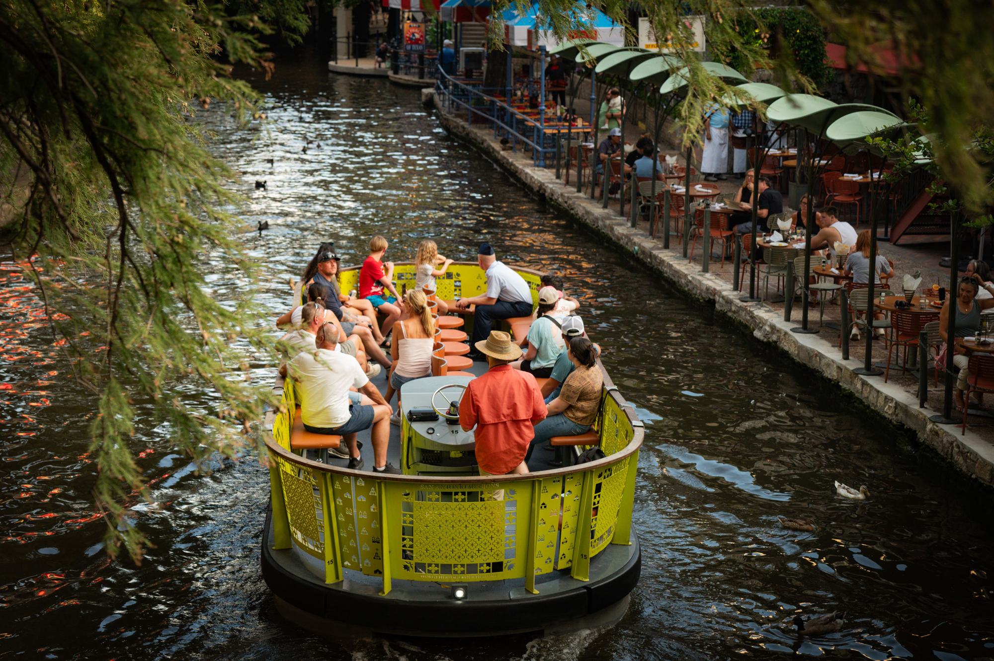 A river barge full of visitors gliding along the shaded San Antonio River Walk
