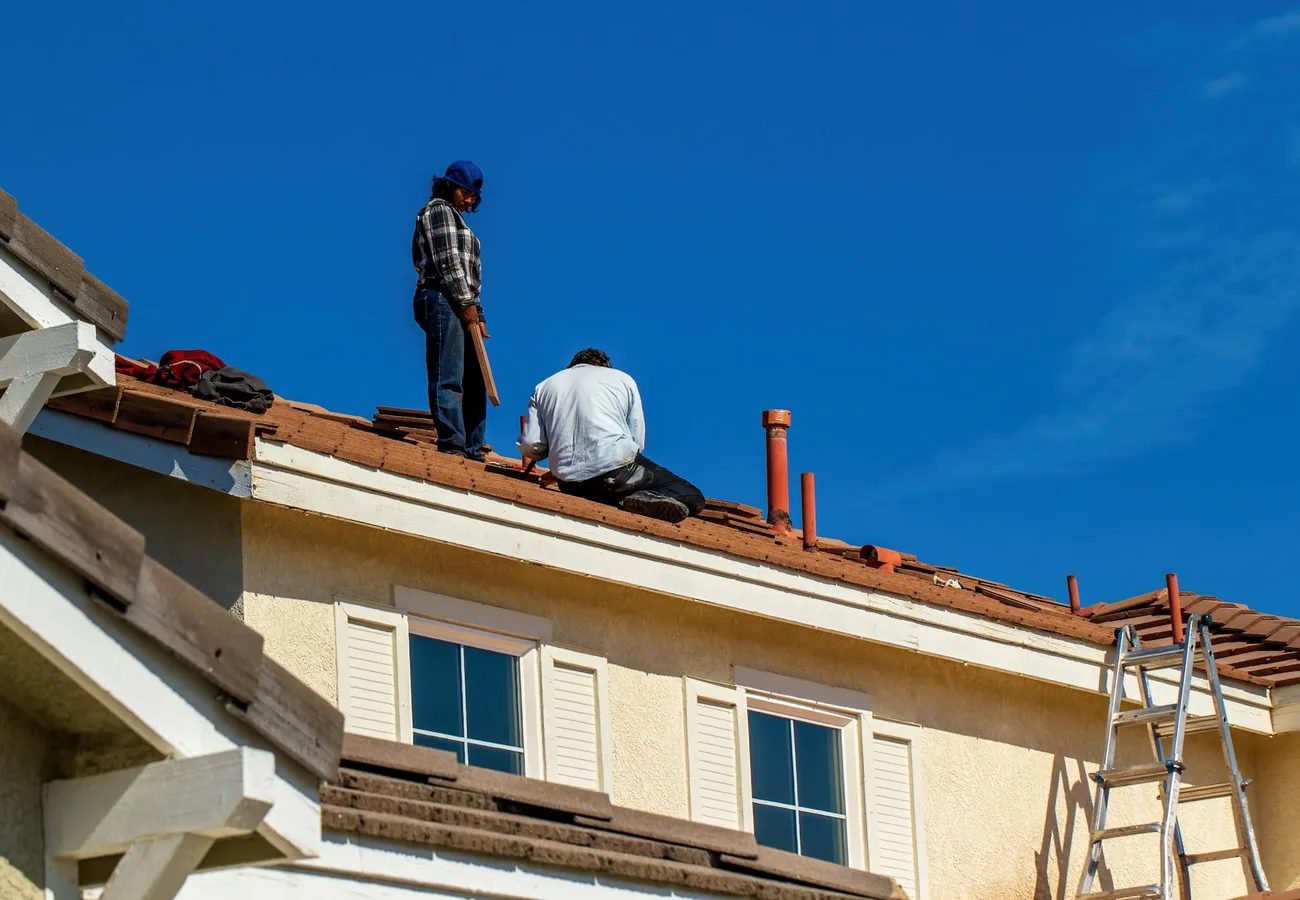 Two roofers working on a tile roof under a clear blue sky