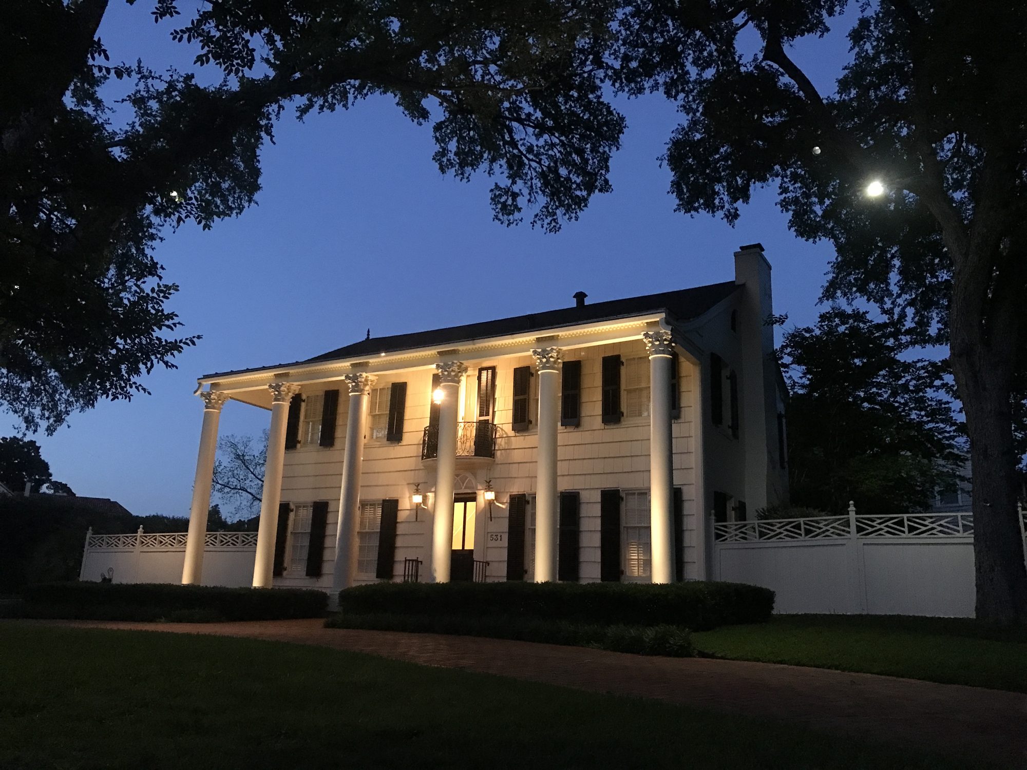 A white columned colonial home in Terrell Hills, lit at dusk beneath live oaks